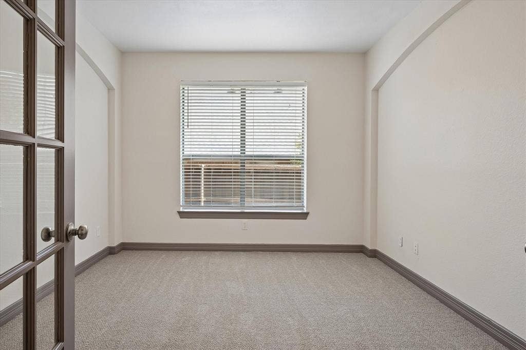 French doors with glass panes, single window with horizontal blinds, neutral wall paint, gray carpeting, and gray baseboards