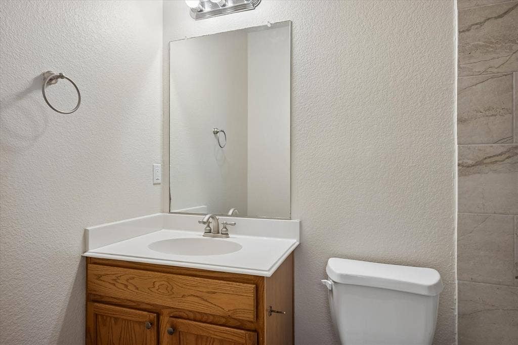 Vanity with wood-finish cabinetry, white countertop, and an integrated sink