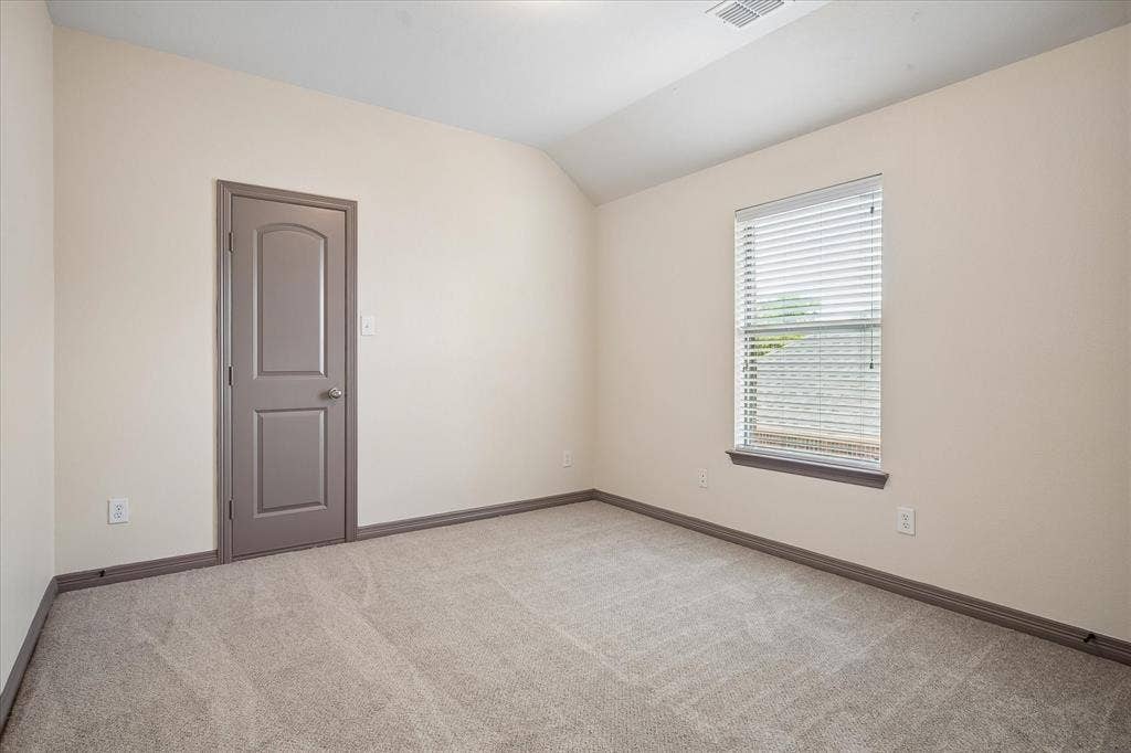 Neutral tone wall paint, vaulted ceiling, light-colored carpet flooring, single window with blinds, and a paneled interior door