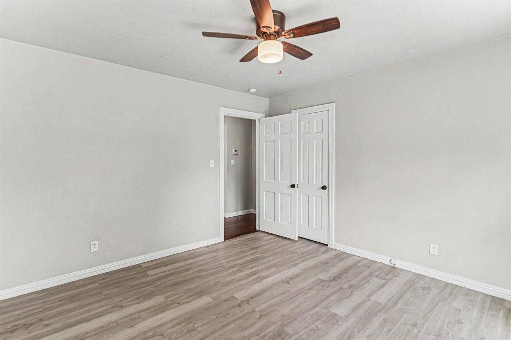 1108 E Robert Street, Fort Worth, TX 76104 Wood-finish flooring, light gray wall paint, white trim, paneled bifold closet doors, and a ceiling fan with integrated lighting