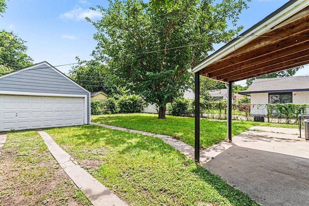 1108 E Robert Street, Fort Worth, TX 76104 Detached two-car garage with panel door, covered carport with paved surface, concrete walkway, and mature trees