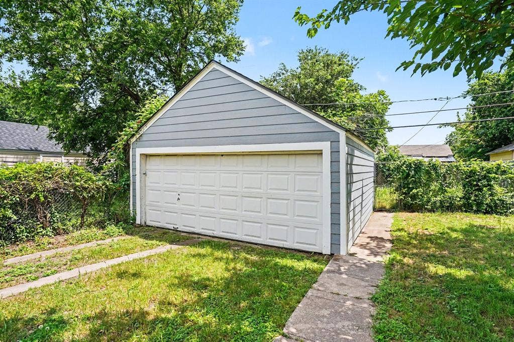 1108 E Robert Street, Fort Worth, TX 76104 Detached garage with horizontal siding, a white panel garage door, and a concrete pathway