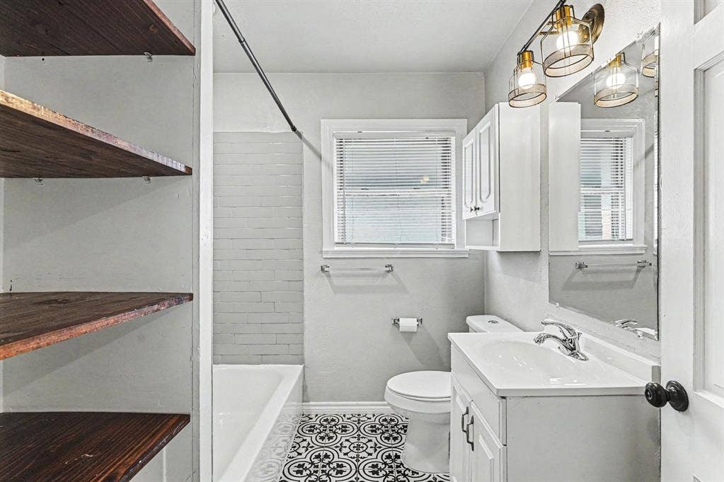 1108 E Robert Street, Fort Worth, TX 76104 Bathroom featuring patterned floor tile, white vanity with integrated sink, built-in open shelving, tub with tile surround, and an overhead light fixture