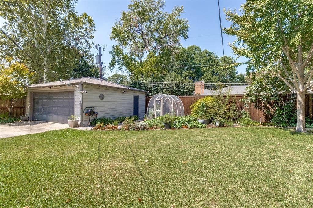6719 Braeburn Drive, Dallas, TX 75214 Expansive grassy yard with a detached garage, a small greenhouse structure, and a wood-paneled fence