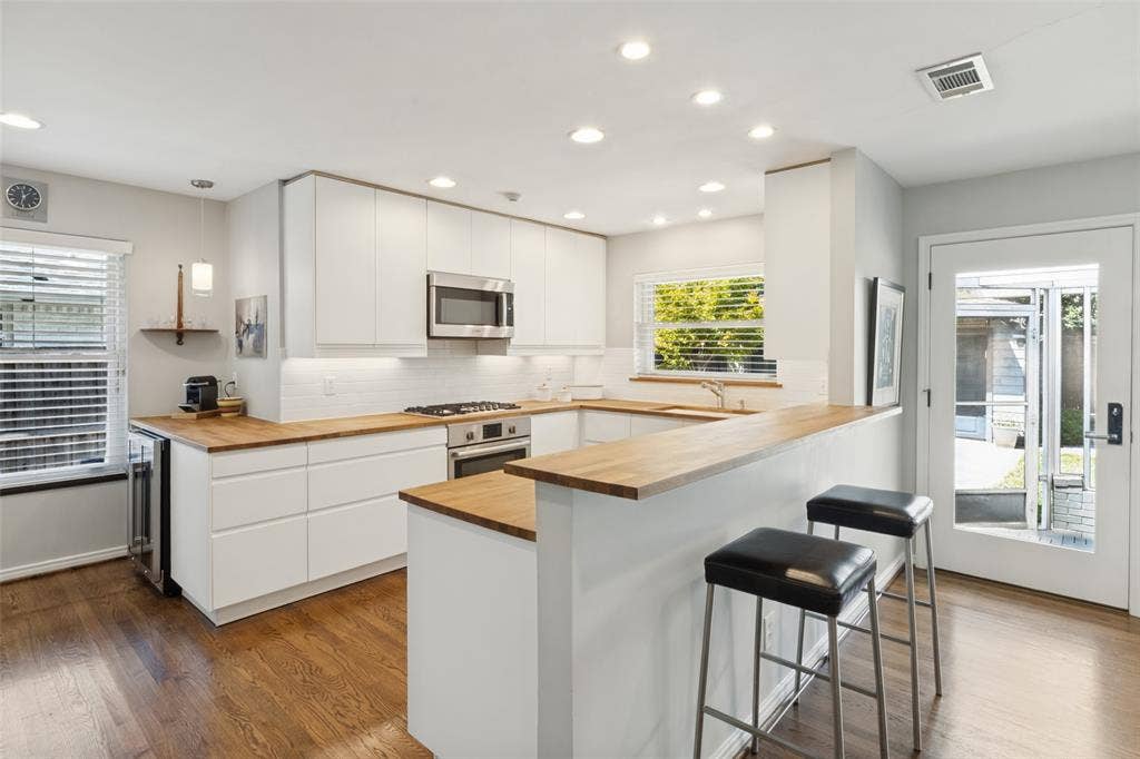 6719 Braeburn Drive, Dallas, TX 75214 U-shaped kitchen featuring wood-finish countertops, white flat-panel cabinetry, stainless steel appliances, a subway tile backsplash, and recessed lighting