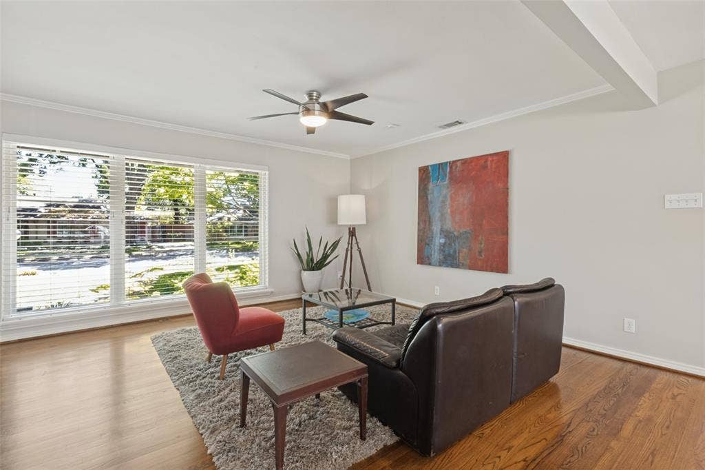 6719 Braeburn Drive, Dallas, TX 75214 Original Hardwood floors, expansive room featuring wood-finish flooring, large windows with blinds, a ceiling fan with integrated lighting, and crown molding