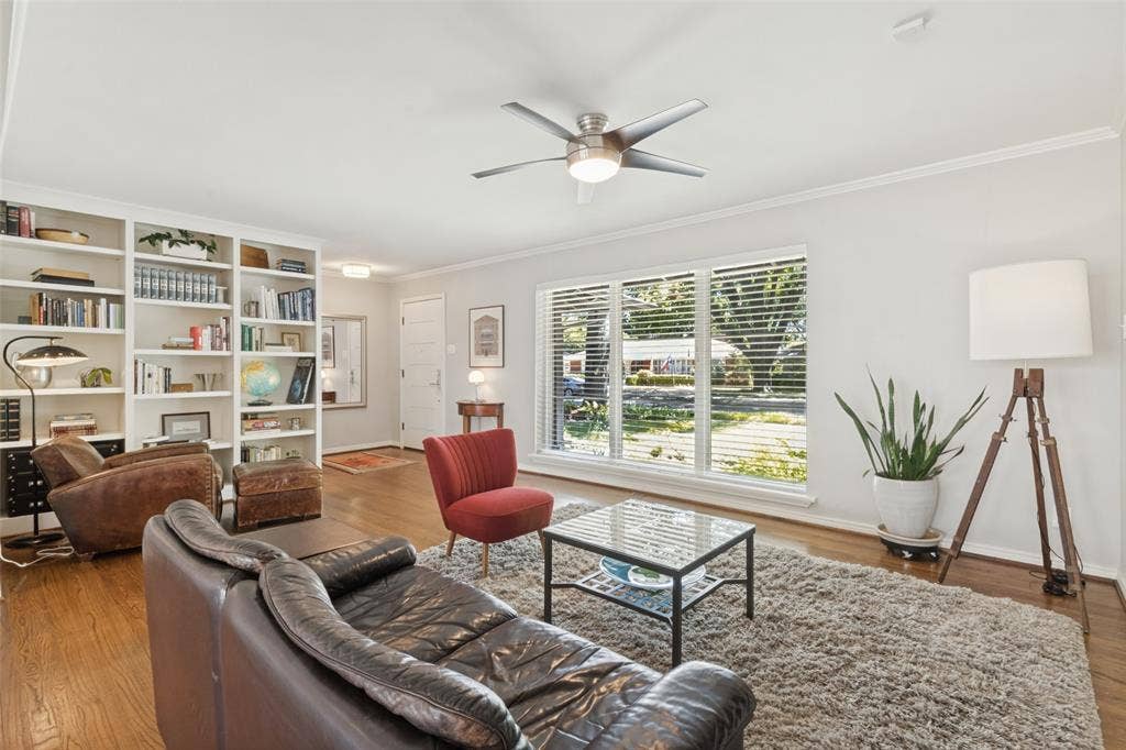 6719 Braeburn Drive, Dallas, TX 75214 Original Hardwood floors, crown molding, white built-in shelving, large windows with blinds, and a ceiling fan with integrated lighting