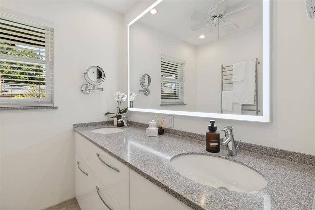 6719 Braeburn Drive, Dallas, TX 75214 Dual undermount sinks with chrome fixtures, a spacious countertop, an illuminated vanity mirror, and a wall-mounted towel warmer