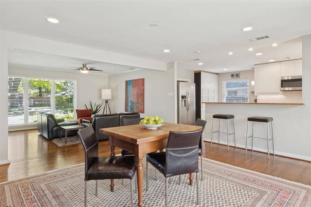 6719 Braeburn Drive, Dallas, TX 75214 Wood-finish flooring throughout, recessed lighting, white kitchen cabinetry, stainless steel appliances, and a kitchen peninsula with bar seating