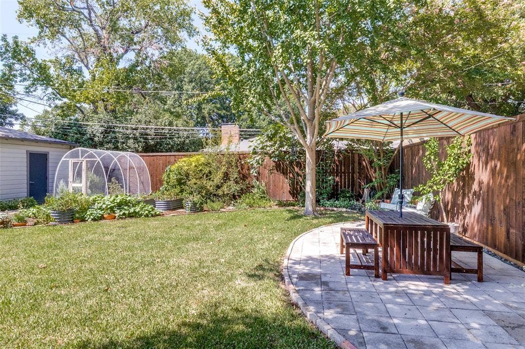 6719 Braeburn Drive, Dallas, TX 75214 Expansive backyard featuring a manicured lawn, established shade trees, a curved paver patio, and a dedicated greenhouse structure