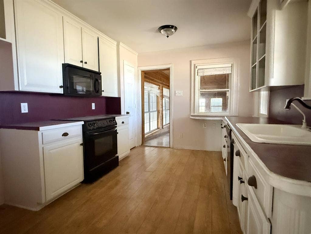 Kitchen featuring wood-finish flooring, white cabinetry, a built-in microwave, and a stainless-steel sink