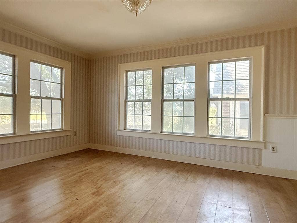 Wood-finish flooring, multiple pane windows, striped wallpaper, wainscoting, and a ceiling-mounted light fixture