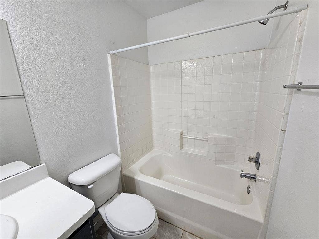 1615 Herald Street, #1613, Dallas, TX 75215 White tiled shower/tub combination with a built-in shelf, adjacent toilet, and vanity with a countertop