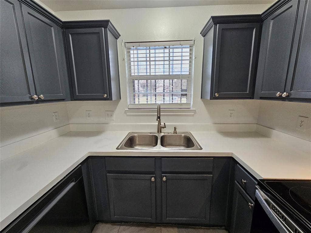 1615 Herald Street, #1613, Dallas, TX 75215 U-shaped countertop with a dual basin stainless steel sink, framed by dark cabinetry and a window with blinds