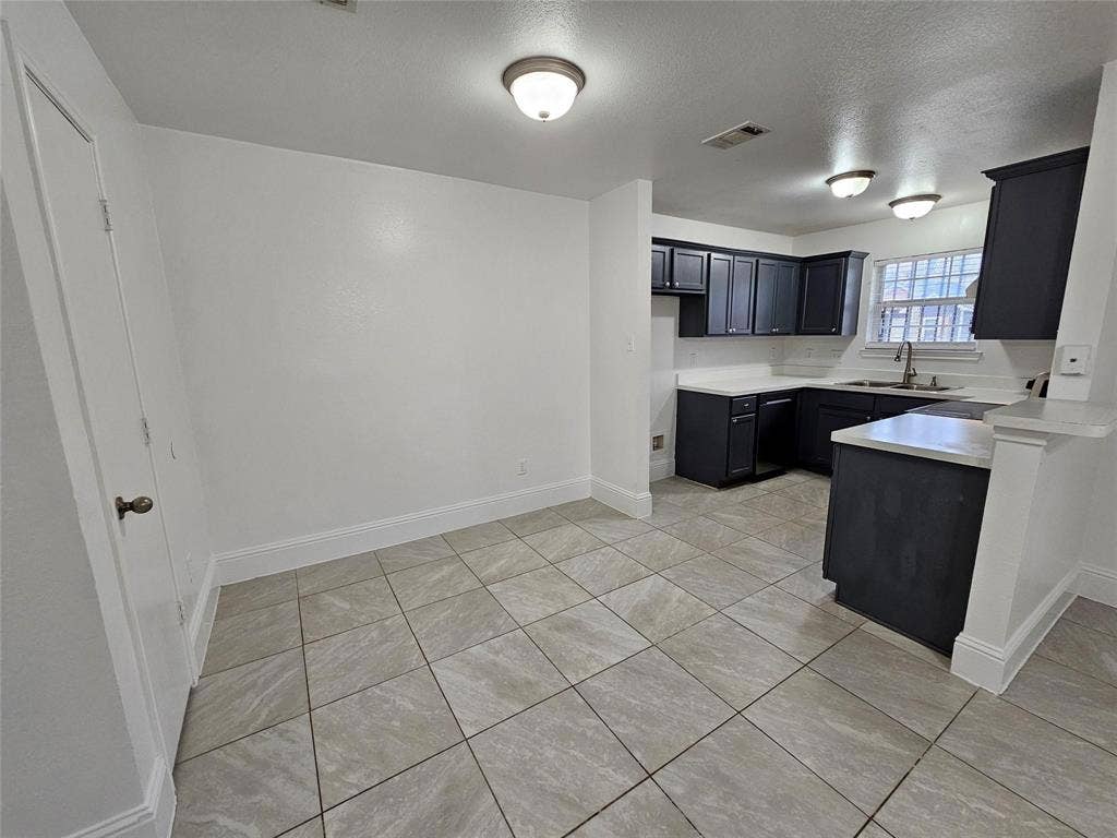 1615 Herald Street, #1613, Dallas, TX 75215 Kitchen and dining area featuring tile flooring, dark cabinetry, light countertops, and a stainless steel sink