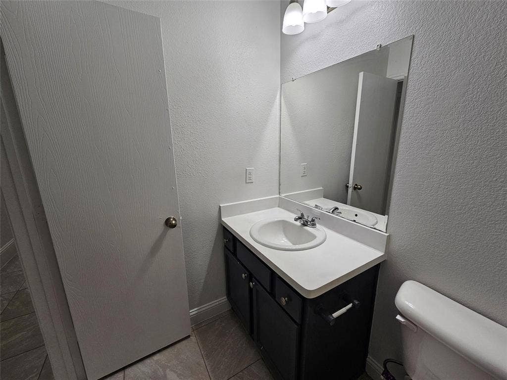 1615 Herald Street, #1613, Dallas, TX 75215 Vanity with a white countertop and integrated sink, chrome faucet, wall-mounted mirror, and tile flooring