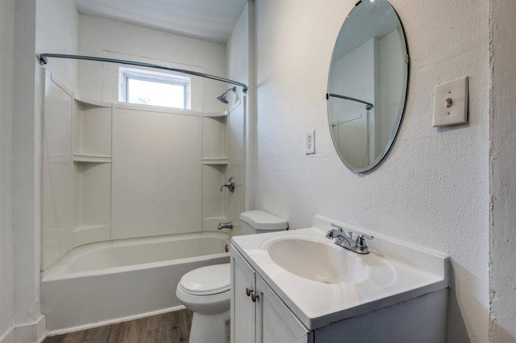 804 Sunset Avenue, #C, Dallas, TX 75208 Bathroom featuring a white vanity with integrated sink, chrome fixtures, oval wall mirror, full-size bathtub with shower, and wood-finish flooring