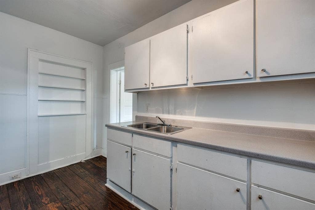 804 Sunset Avenue, #C, Dallas, TX 75208 White cabinetry with chrome hardware, dual basin stainless steel sink, light-toned countertop, and built-in wall shelving