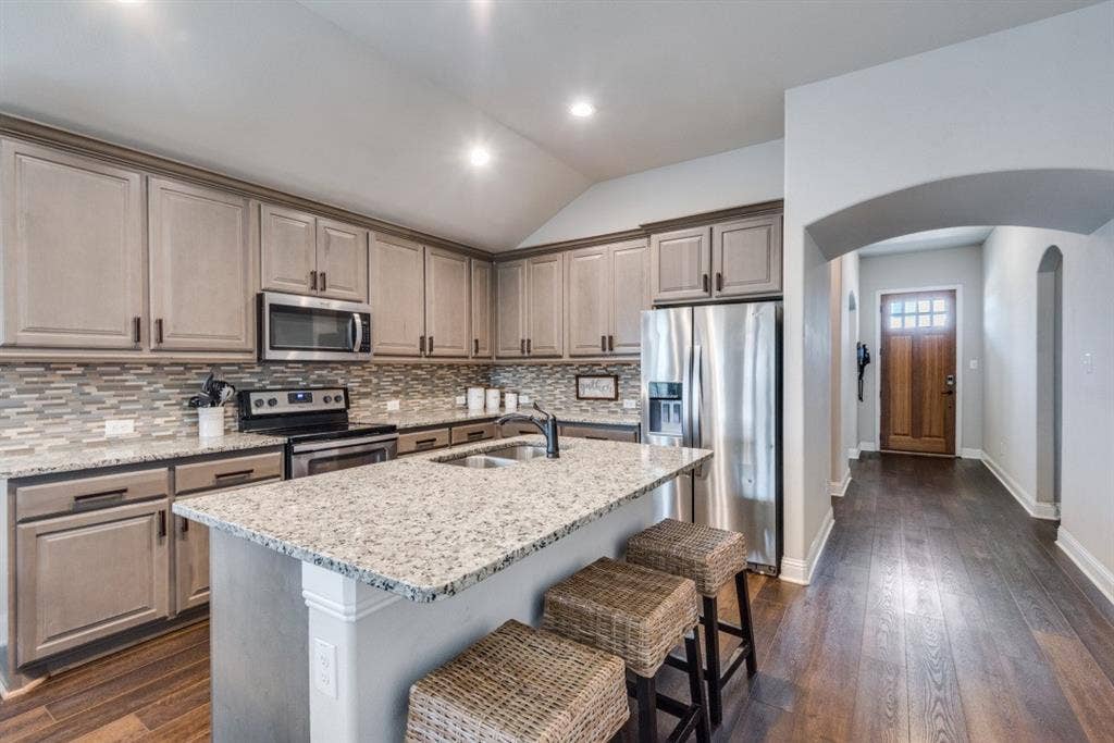 6911 Truth Drive, Dallas, TX 75236 Kitchen featuring a large island with stone countertops, stainless steel appliances, extensive cabinetry, and a mosaic tile backsplash