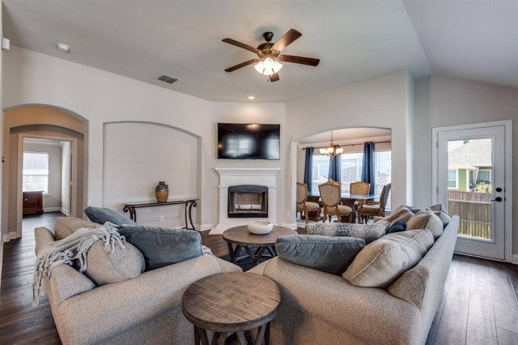6911 Truth Drive, Dallas, TX 75236 Vaulted ceiling with a ceiling fan, fireplace with a white mantel, arched doorways, wood-finish flooring, and a glass-paneled exterior door