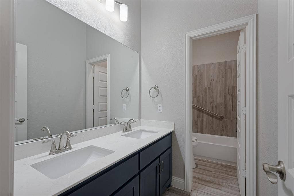 6001 Allison Drive, Midlothian, TX 76065 The hall bath features dual undermount sinks with brushed nickel faucets, non-natural quartz-finish countertop, oversized wall mirror and tile flooring. The private bathing area features a grab bar and and pull down seat.
