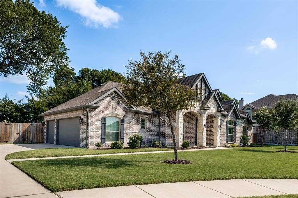 6001 Allison Drive, Midlothian, TX 76065 Brick and stone exterior with arched entryway, dark shingles, side entry three-car garage and manicured lawn.