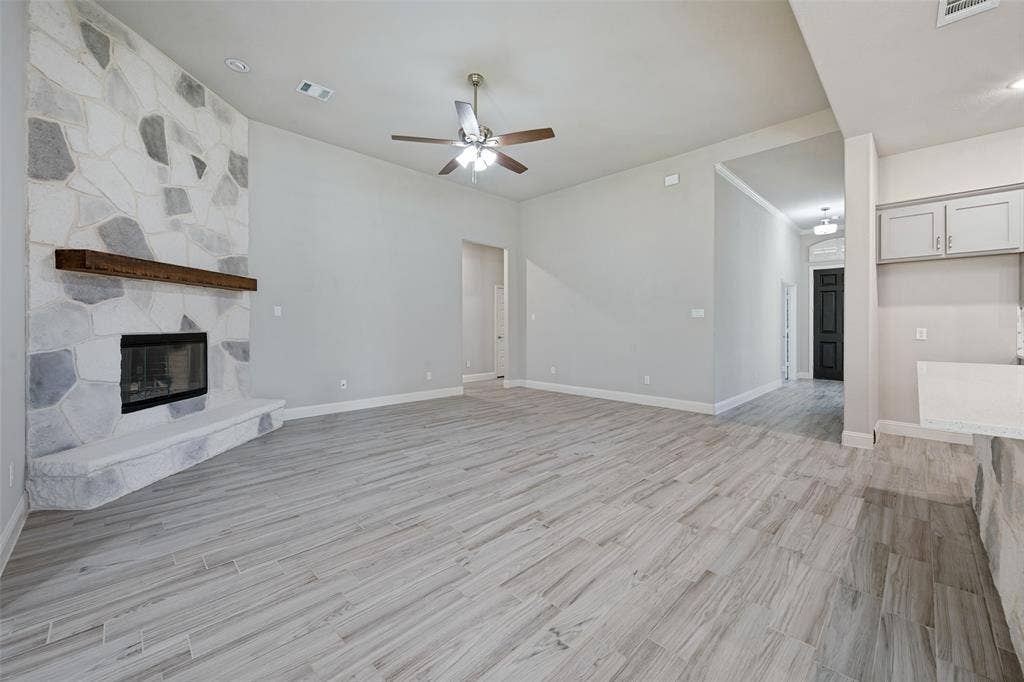 6001 Allison Drive, Midlothian, TX 76065 Spacious living area featuring a blown in stone facade fireplace with a wood mantel, light-toned wood-look tile flooring and a ceiling fan and light which are controled with a remote.