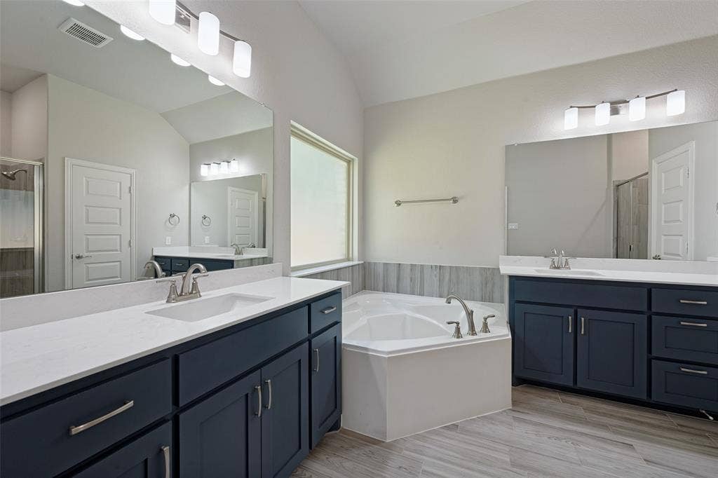 6001 Allison Drive, Midlothian, TX 76065 Dual vanities with white countertops, deep blue cabinetry, corner soaking tub, and wood-look tile flooring grace the ensuite bathroom. And look at the drawer space!