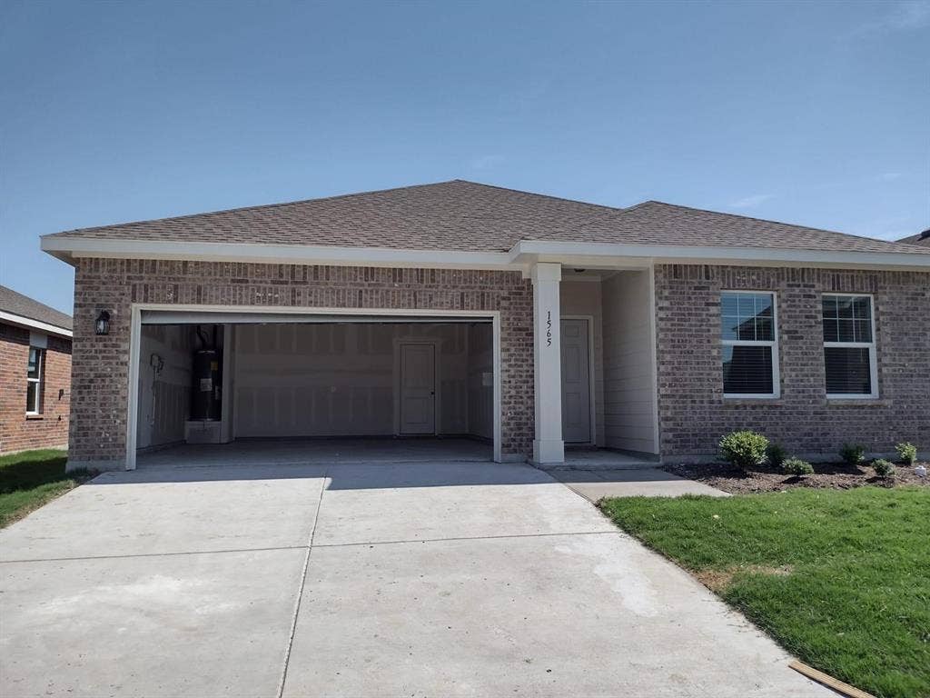 Brick exterior with an attached garage, covered entry, front landscaping, and a concrete driveway