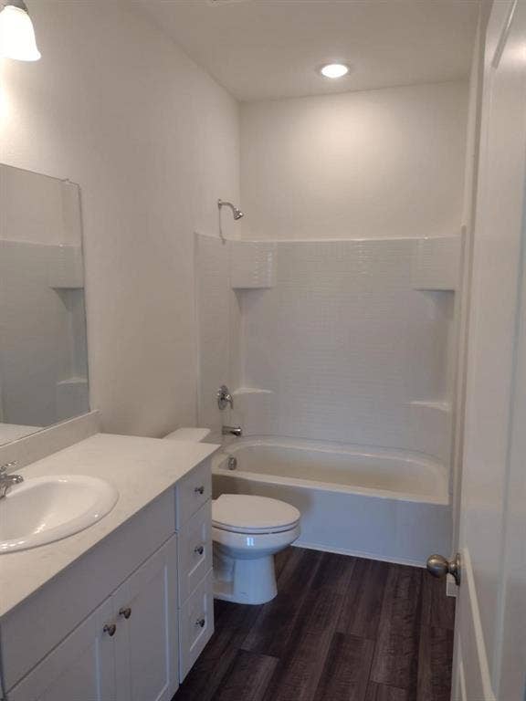 Vanity with integrated sink, wood-finish flooring, white bathtub with shower, recessed ceiling light, and wall-mounted light fixture
