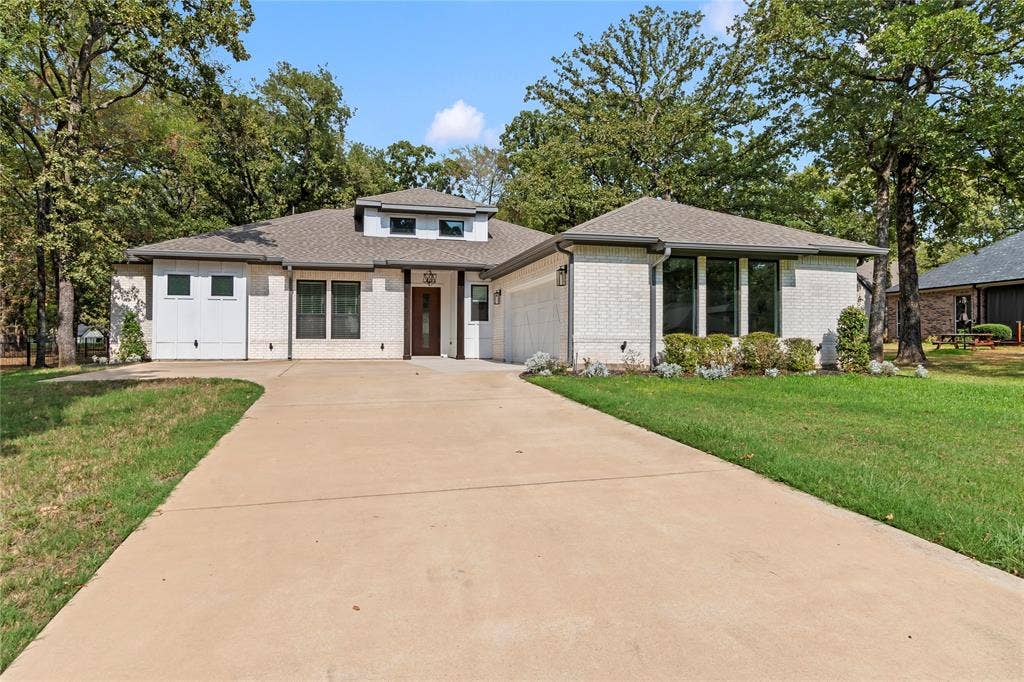 128 Saint Andrews Drive E, Mabank, TX 75156 Contemporary exterior with light-colored brick, a dark wood-finish entry door, multiple large windows, and a concrete driveway