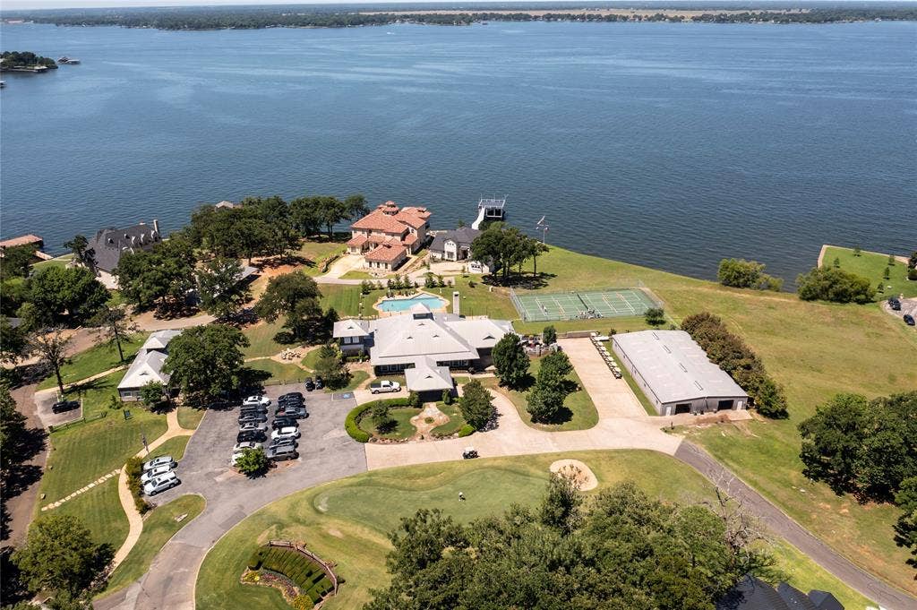 128 Saint Andrews Drive E, Mabank, TX 75156 Expansive property featuring a waterfront setting, private tennis courts, an in-ground swimming pool, a golf course putting green, and a large multi-vehicle parking area