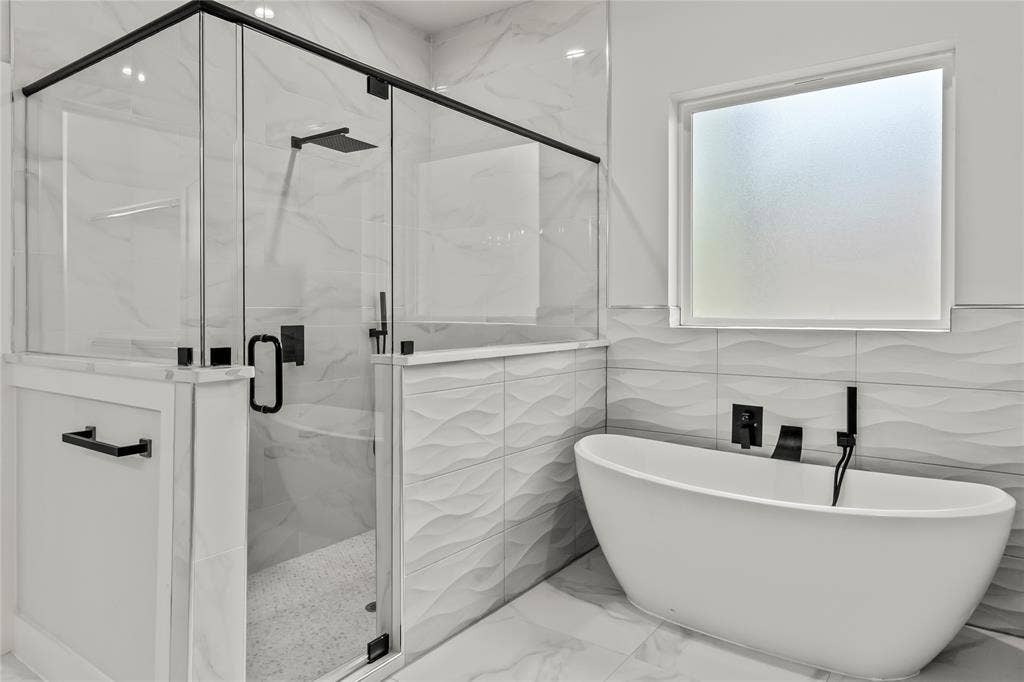 128 Saint Andrews Drive E, Mabank, TX 75156 Freestanding soaking tub with matte black fixtures, separate glass-enclosed shower with matte black hardware, textured wall tiles, and large format floor tiles