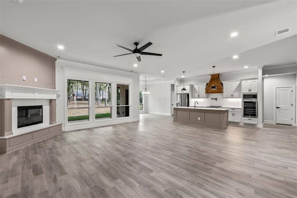 128 Saint Andrews Drive E, Mabank, TX 75156 Open-concept living area featuring wood-finish flooring, a white mantel fireplace, and a kitchen with white cabinetry, a center island, and a wood-hood range