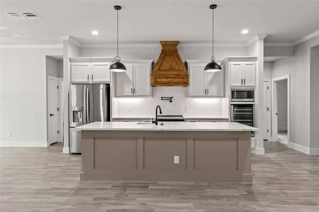 128 Saint Andrews Drive E, Mabank, TX 75156 Spacious kitchen featuring a central island with a light-toned base and a white countertop, stainless steel appliances, a decorative wood range hood, and pendant lighting