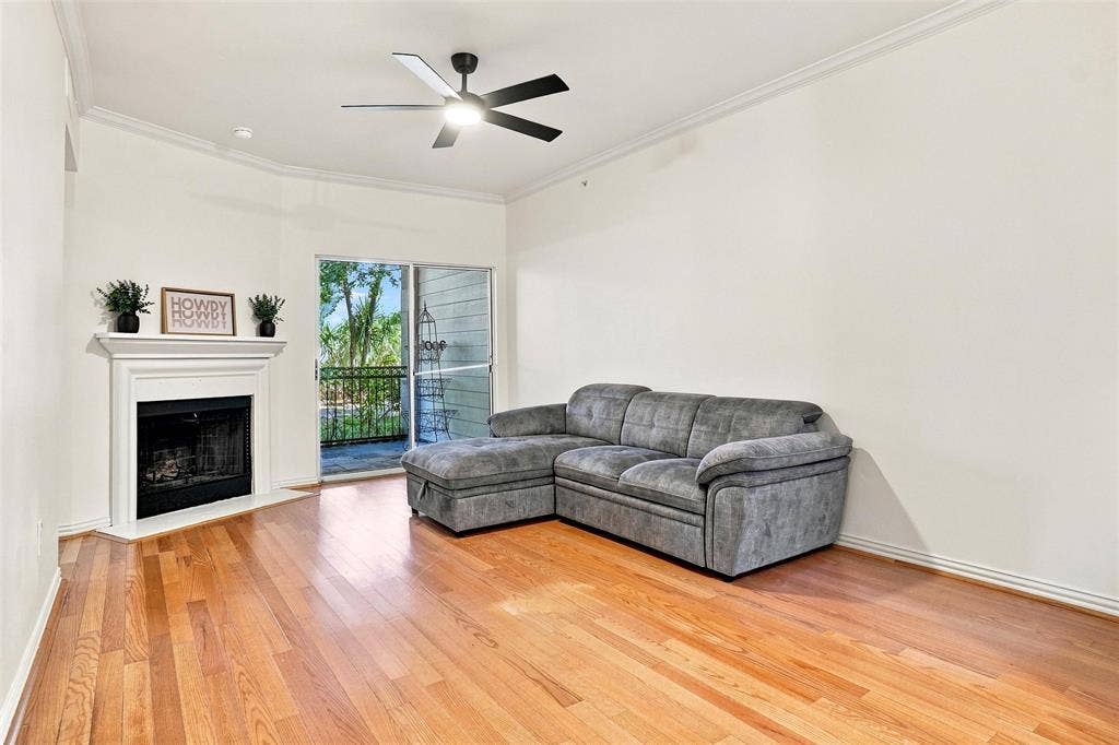 2601 Preston Road, #4103, Plano, TX 75093 Hardwood flooring, corner fireplace with white mantel, ceiling fan, crown molding, and sliding glass door to a balcony with black railings