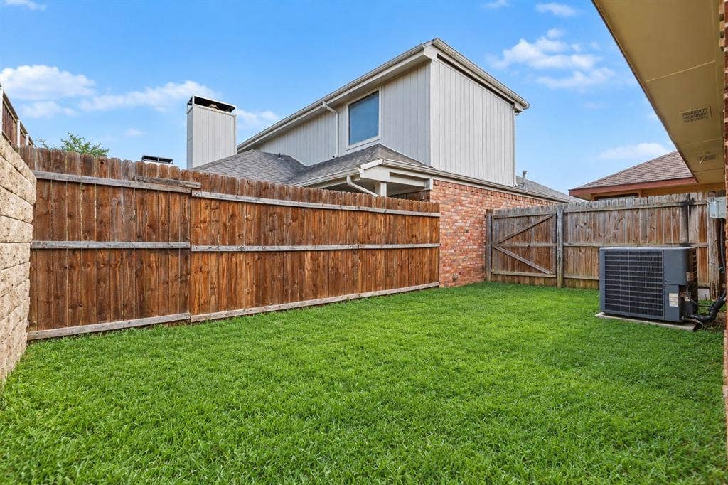 Enclosed backyard featuring a wood privacy fence, green lawn, and exterior brick accents