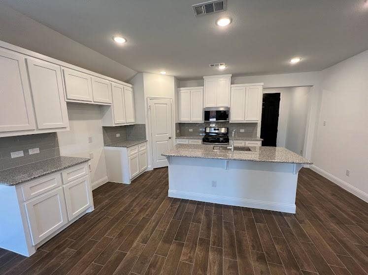 1408 Rendyn Street, Anna, TX 75409 Open-concept kitchen featuring white cabinetry, light-toned countertops, a central island with an integrated sink, modern stainless steel appliances, and wood-finish flooring