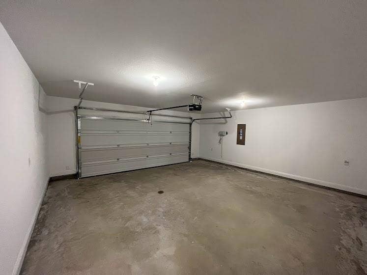 1408 Rendyn Street, Anna, TX 75409 Enclosed garage with a white sectional door, exposed overhead door mechanism, concrete flooring, and ceiling-mounted lighting