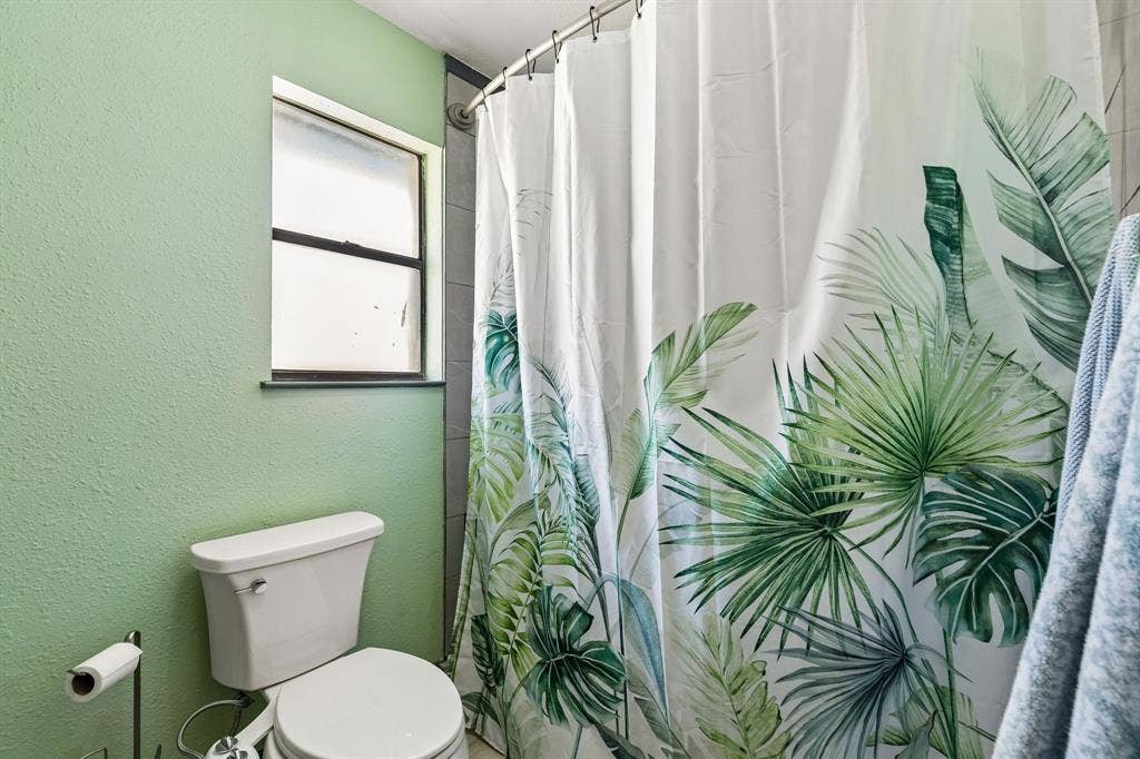 Compact bathroom with a two-piece toilet, tiled shower surround, and a window for natural light