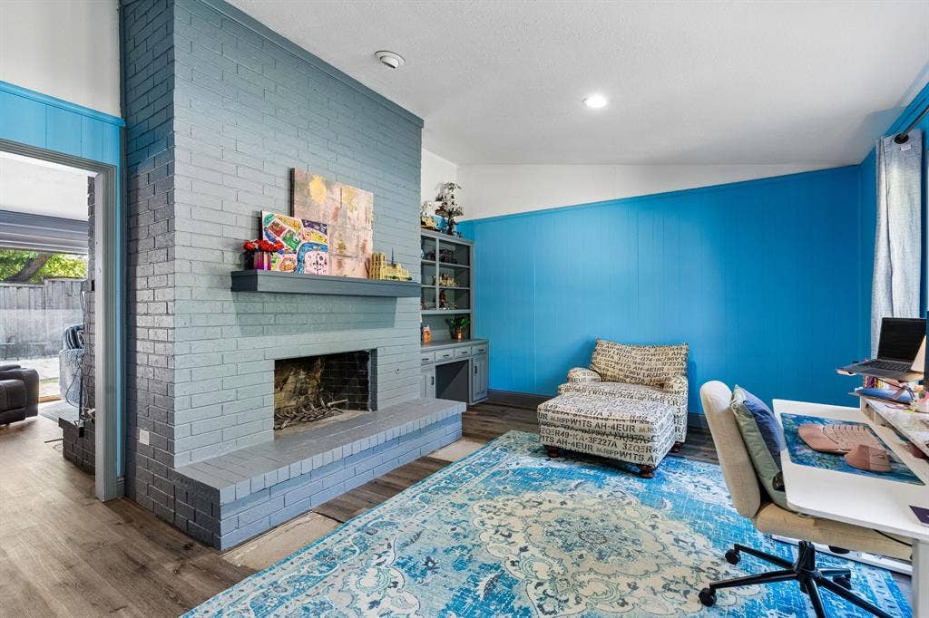 Brick fireplace with a substantial hearth and mantel, wood-finish flooring, recessed lighting, and built-in cabinetry with glass-front uppers