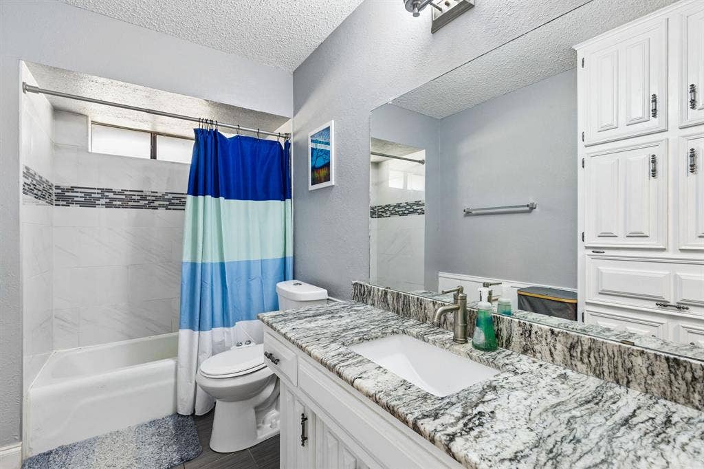 Bathroom featuring a white vanity with an integrated sink, patterned countertop, wall-mounted mirror, and white cabinetry