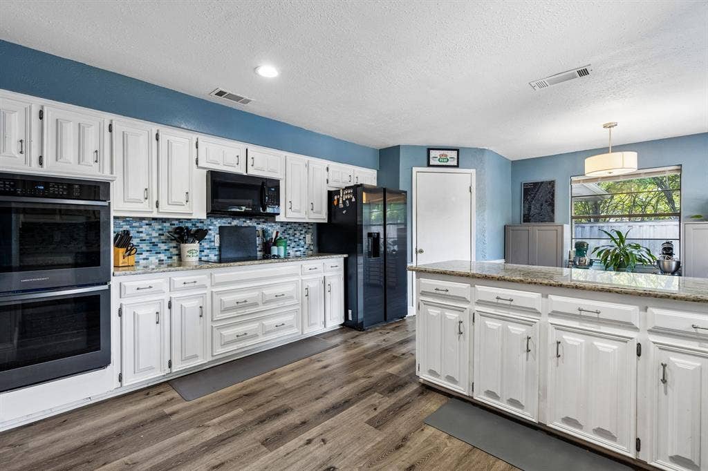 Kitchen with white cabinetry, wood-finish flooring, a mosaic tile backsplash, a double wall oven, and a center island with a stone countertop