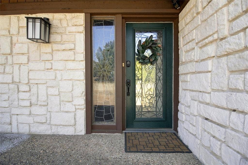 1417 Sun Valley Drive, Garland, TX 75043 Stone-clad exterior with an ornate glass-paneled front door, an adjacent sidelight, and an exterior wall lantern