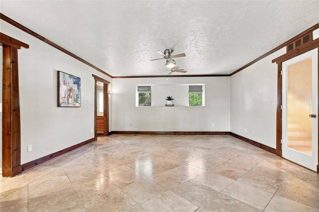 1417 Sun Valley Drive, Garland, TX 75043 Another view of the primary bedroom with neutral-toned tile flooring, two ceiling fans, white walls with dark wood trim, and a door with a frosted glass panel