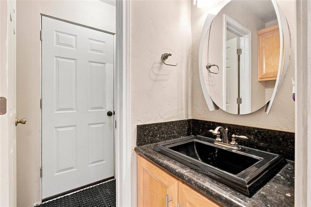 1417 Sun Valley Drive, Garland, TX 75043 Half bathroom with black rectangular undermount sink with a two-handle faucet, set into a dark stone countertop with a matching backsplash