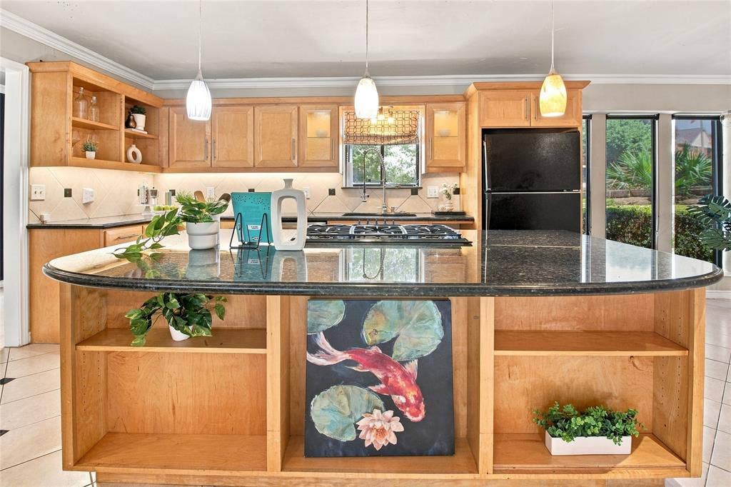 1417 Sun Valley Drive, Garland, TX 75043 Kitchen featuring light wood cabinetry, a dark granite-style island with built-in shelving, a gas range, and a black refrigerator