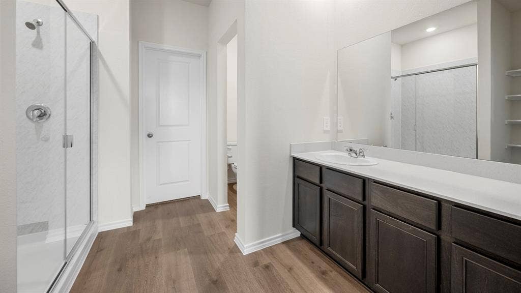 5033 Shumard Drive, Lindale, TX 75771 Wood-finish flooring with a glass-enclosed shower, dark wood vanity with a white countertop, and expansive wall-mounted mirror