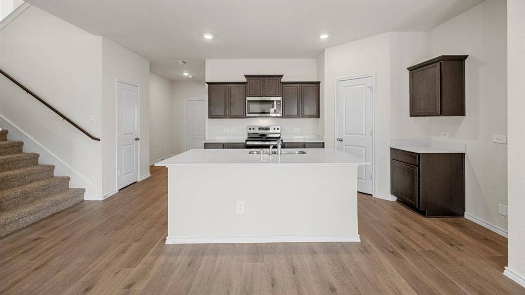 5033 Shumard Drive, Lindale, TX 75771 Kitchen featuring dark wood-finish cabinetry, white countertops, a stainless steel microwave, and a kitchen island with an integrated sink