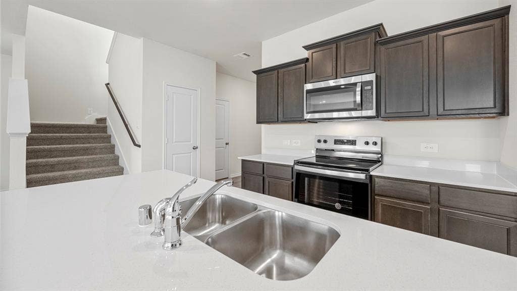 5033 Shumard Drive, Lindale, TX 75771 Kitchen featuring a double basin stainless steel sink, stainless steel appliances, dark wood-finish cabinetry, and light-colored countertops